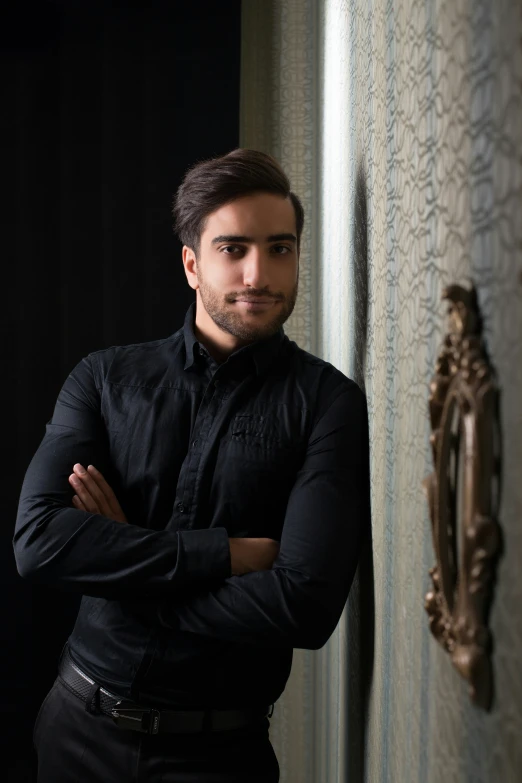 a man leaning against a wall wearing a black shirt