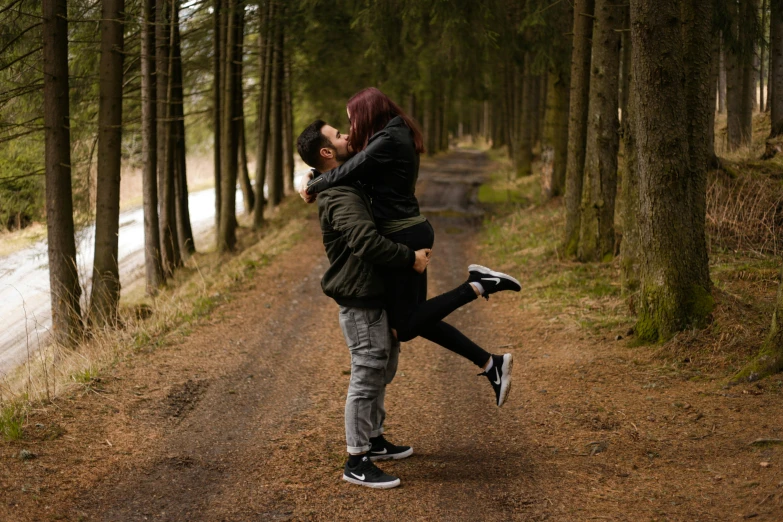 an attractive couple posing on a dirt road with tall trees