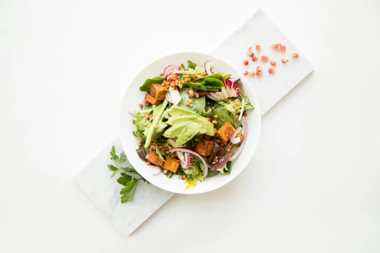 a white plate with a salad topped with lettuce, tomatoes and avocado