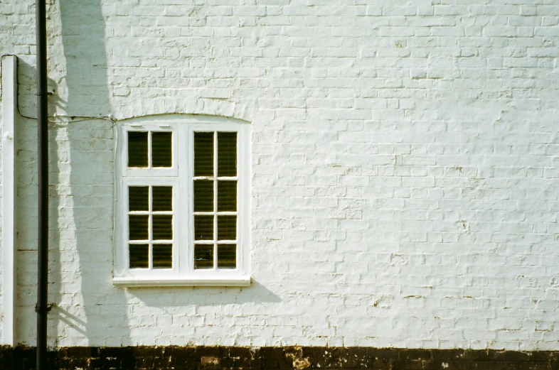 the side of an old, white building with a window on one wall and no glass in the middle of the frame