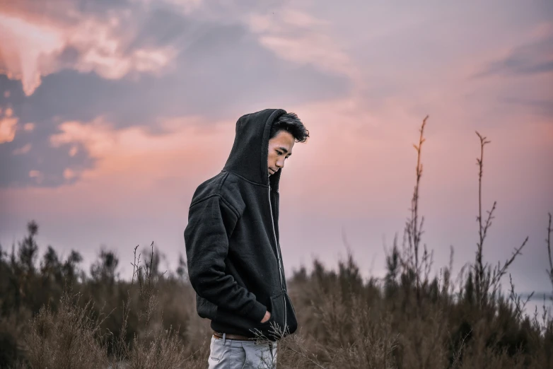 a man standing alone in a field with the sun setting