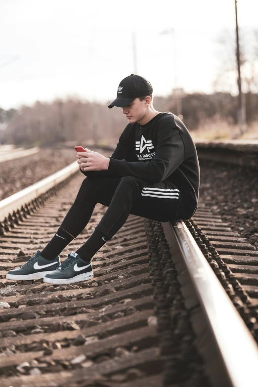a man sitting on train tracks and wearing a hat