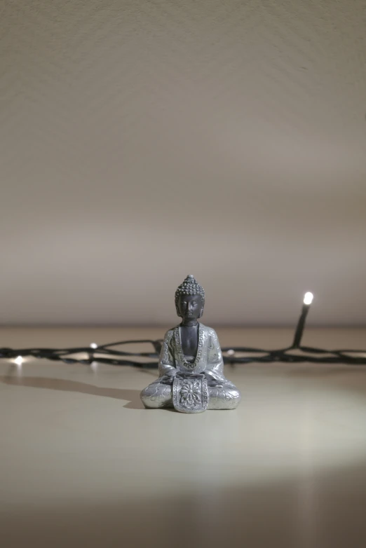 a buddha statue sits on the floor and is lit up by string lights