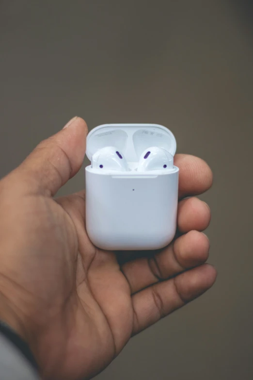 a person is holding a white case that has two wireless earbuds in it