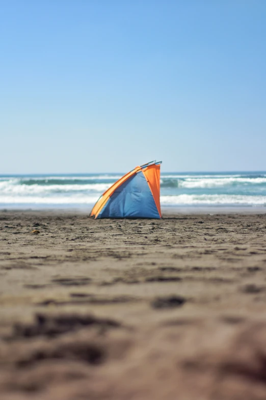 an orange and blue tent sitting on top of a beach