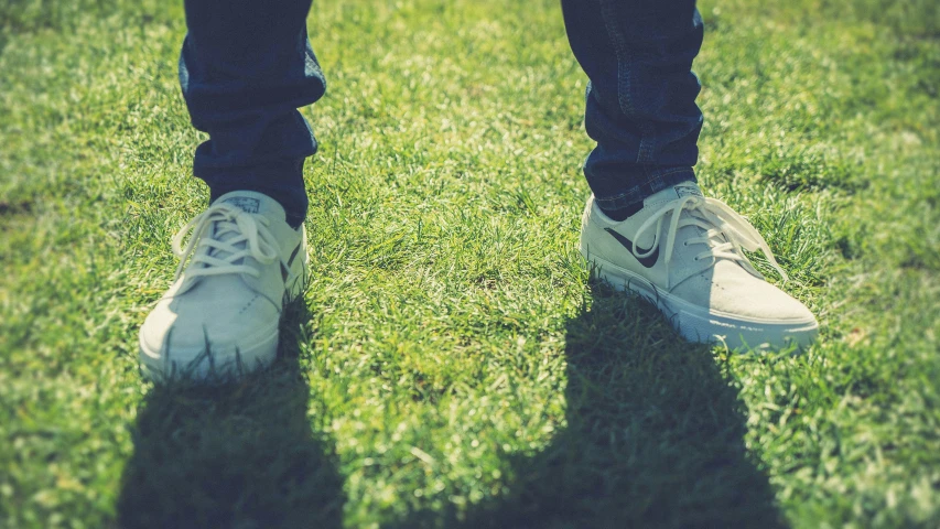 shadow of a person wearing white tennis shoes in the grass