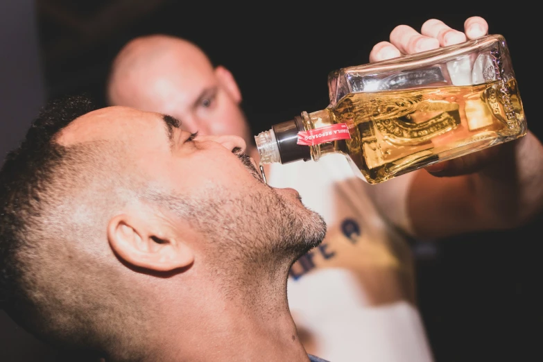 a man drinking soing from a bottle next to another man