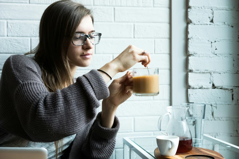 a woman in glasses is holding up a glass of brown liquid