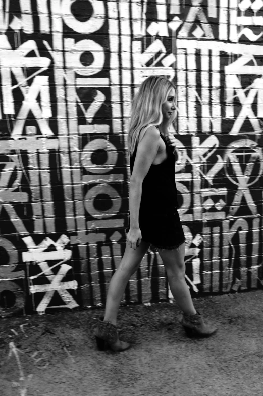 black and white po of a woman walking by a wall covered in letters