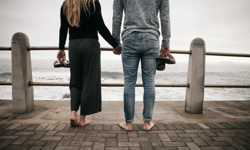 a couple holding hands as they stand together on a railing overlooking the ocean