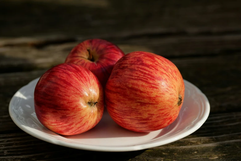 three apples on a white plate with wood background