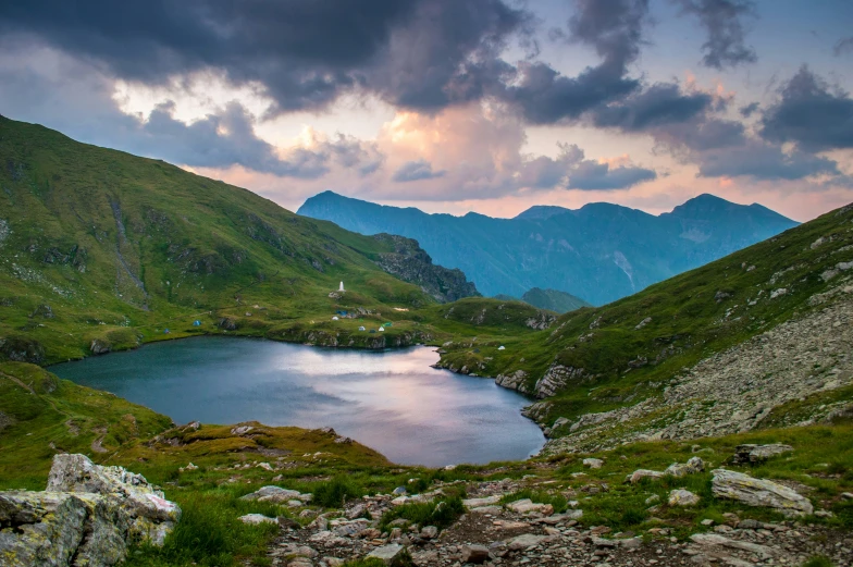 lake and grassy mountains at sunset with dramatic clouds