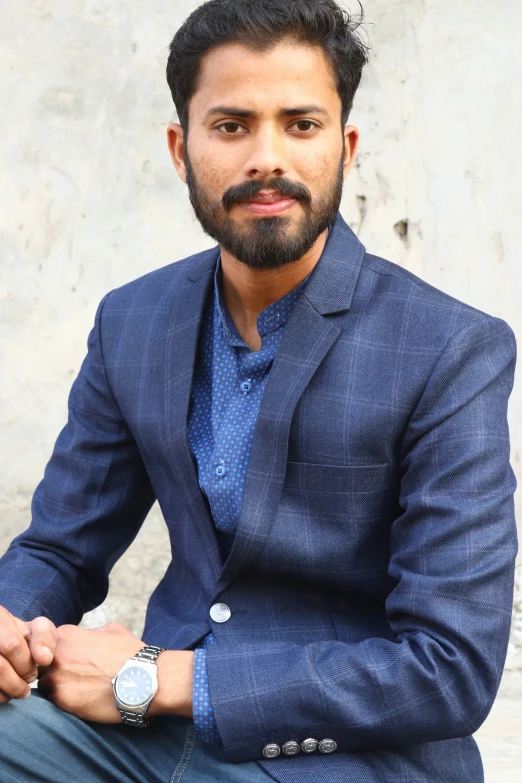 a bearded man in a blue suit is sitting