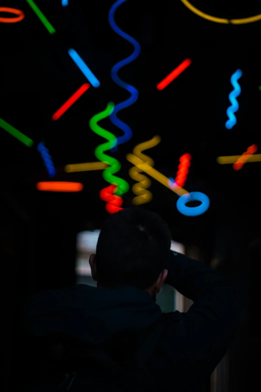 a man is looking up at a wall filled with neon lights