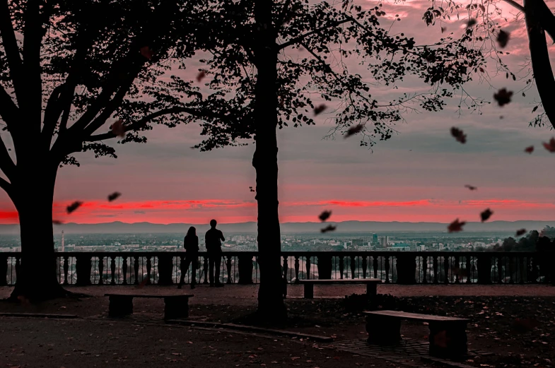 a red sky over a sunset with two people and a bench