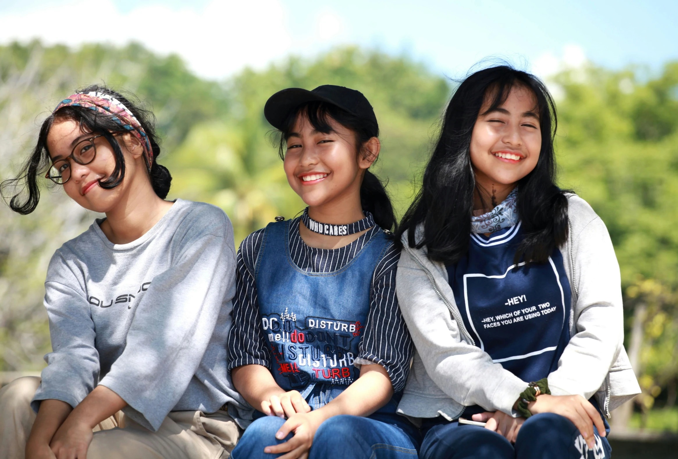 three asian girls wearing blue shirts and denim overalls sitting next to each other