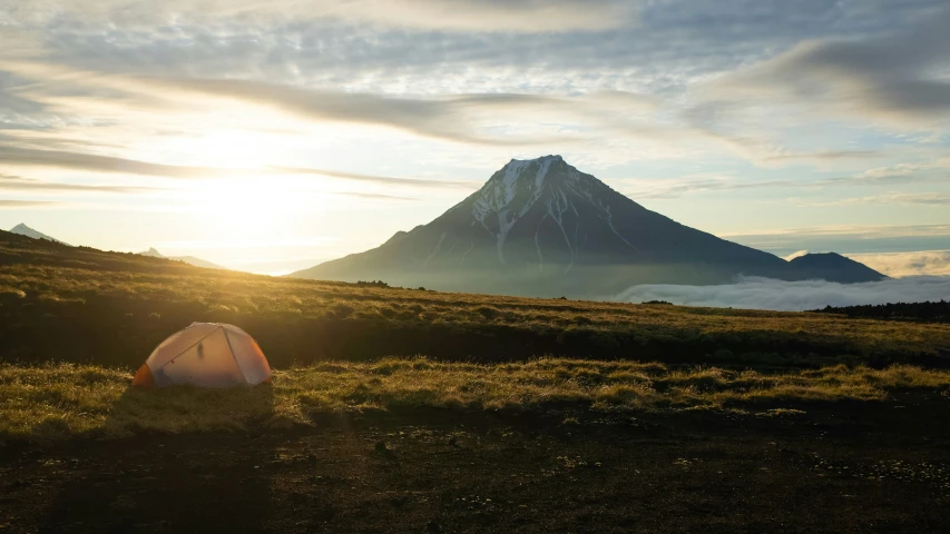 a tent is sitting on a hillside with mountains in the distance