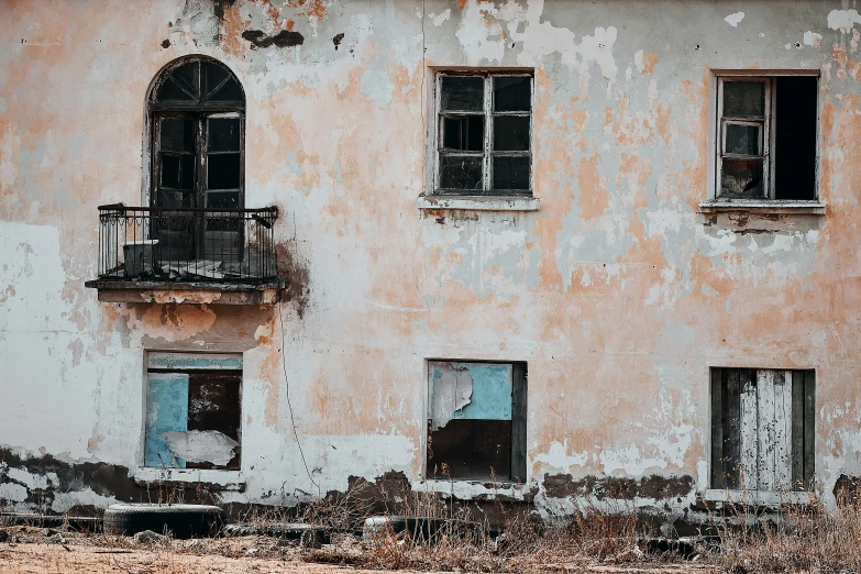 a worn out building with three windows and an old rusted metal fence