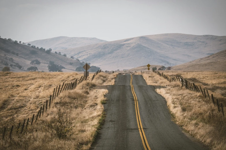 a rural road with some hills and grass on both sides