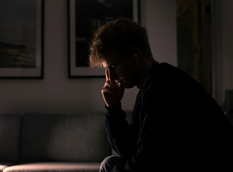 man sitting in the dark while smoking and looking down