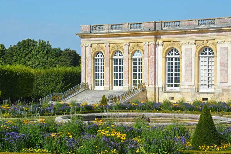 a formal garden with a fountain and stairs leads to several windows and a lot of colorful flowers