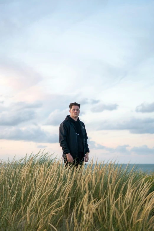 man standing in grass with blue sky and clouds in background