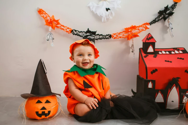 a  in a witch costume sitting on the ground near halloween decorations