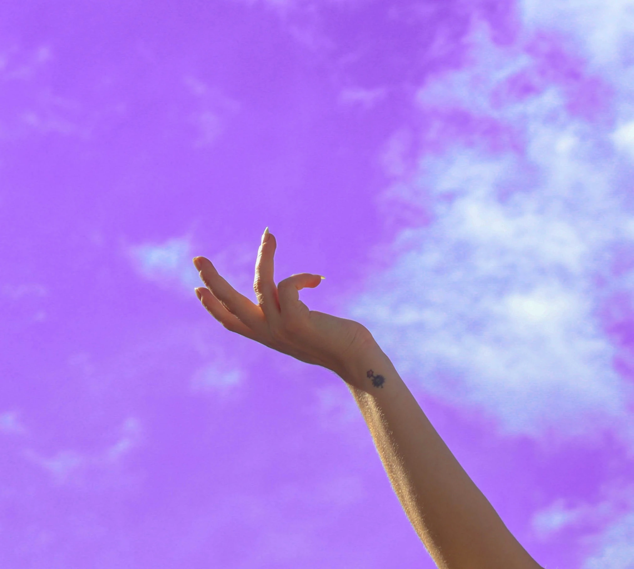 someone's hand reaching into the sky against a purple cloudy sky