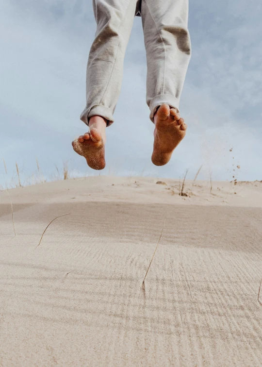 person in sneakers and jeans balancing on sand with blue sky background