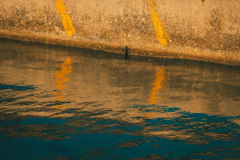 an orange sign is on the side of a wall that is reflecting off the water