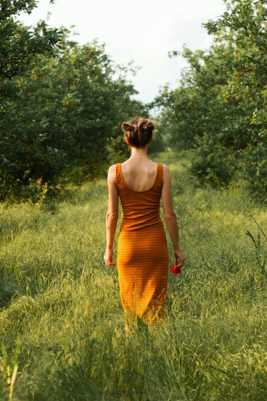 a woman in an orange dress walking through some trees