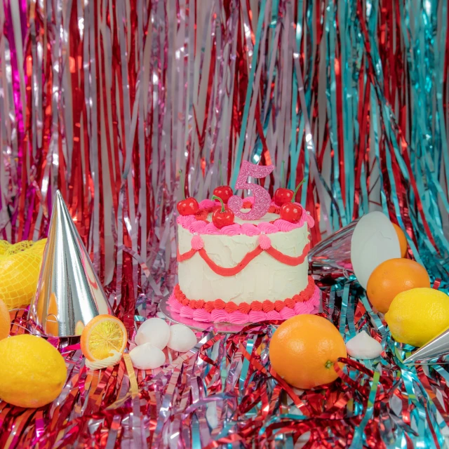 a birthday cake sits atop a table full of fruit and confetti