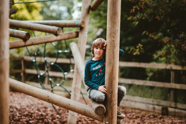 a little boy at the park is leaning against the wooden fence