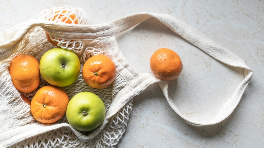 a bag with fruit sitting next to oranges on a table