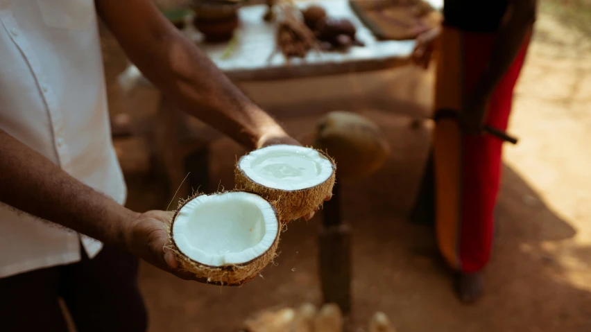 two people standing holding two coconuts near a wooden table