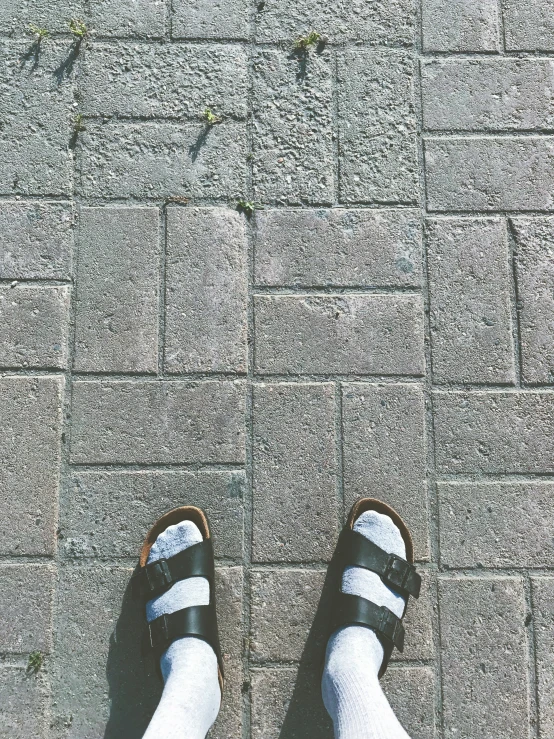 someone with their feet crossed on concrete and wearing black sandals