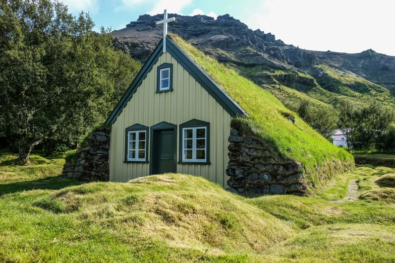 a little green cottage sitting on the side of a hill