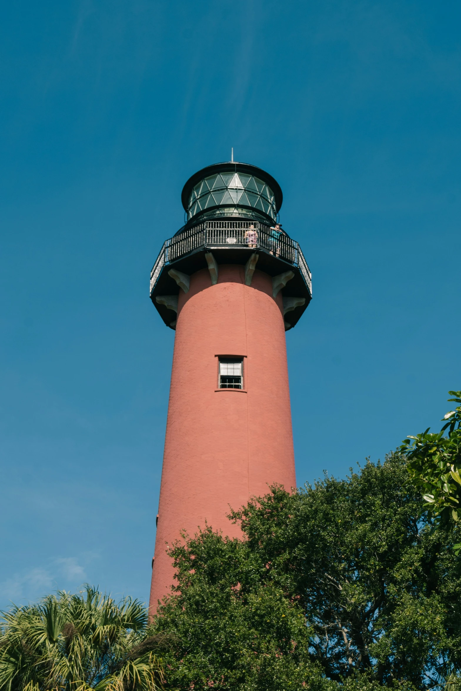 the large red lighthouse is near trees and a clear blue sky