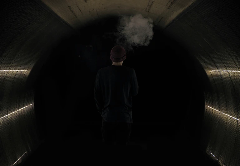 a man in black is walking inside a black tunnel with smoke