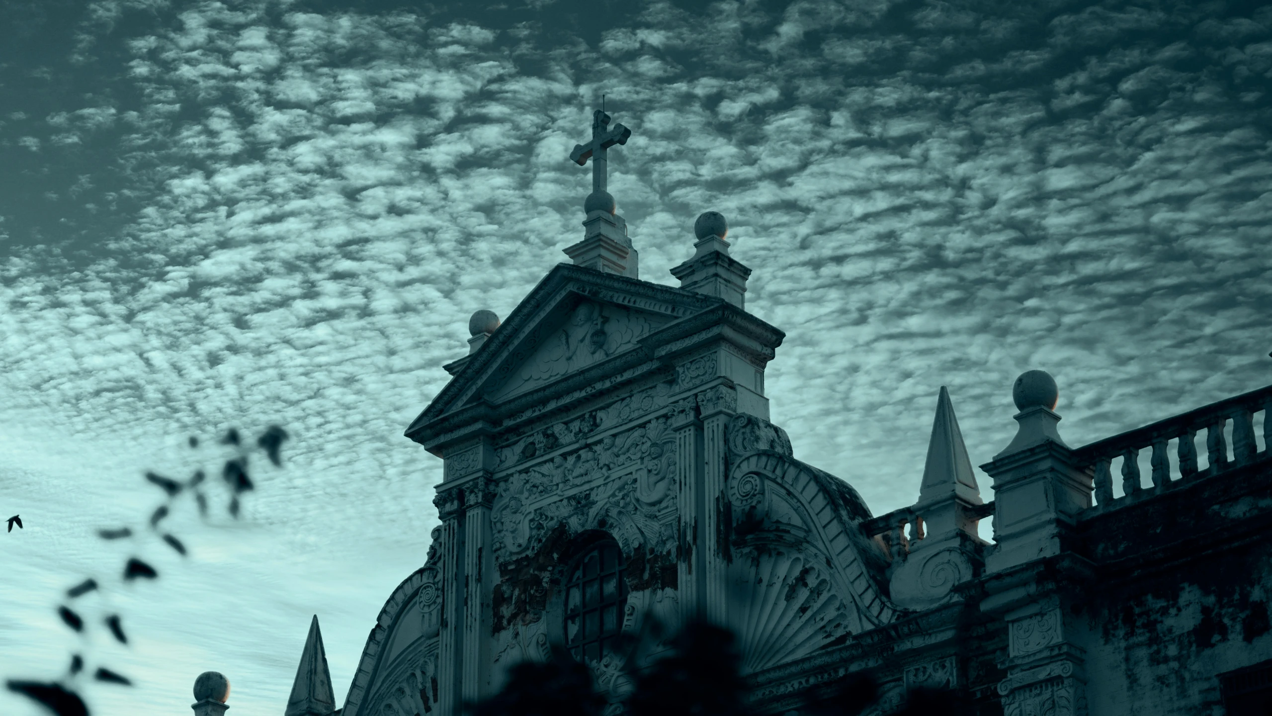 the steeple of a gothic styled church is silhouetted by the cloudy sky