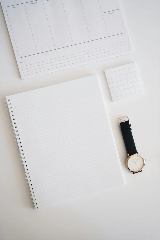 a blank note pad with watch beside it