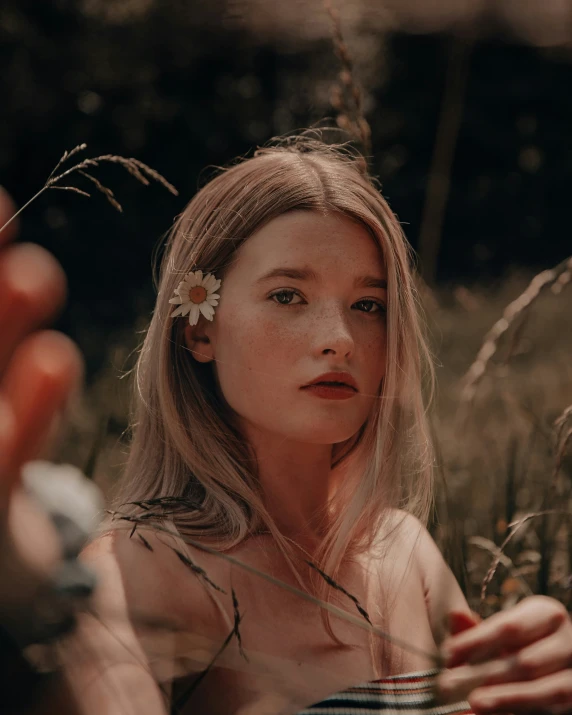 a woman standing in some tall grass with a flower in her hair