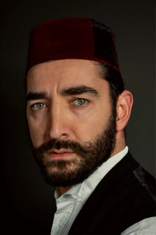 a bearded man with a red hat and black vest