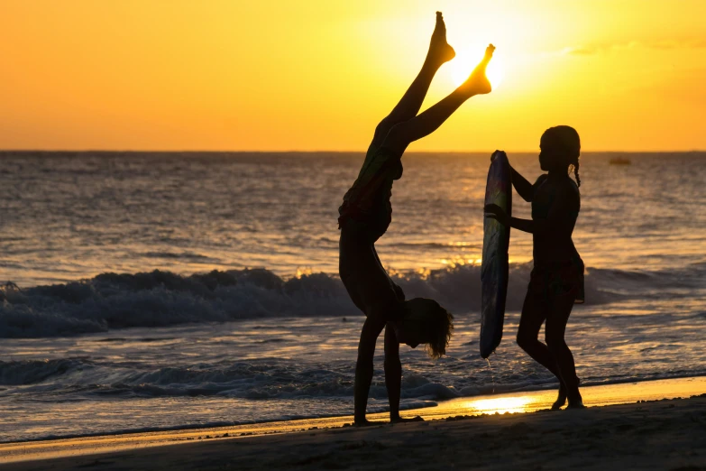 two girls are doing acrobatic on the beach at sunset
