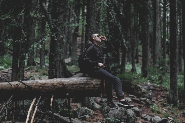 a man sitting on top of a tree log in the middle of a forest