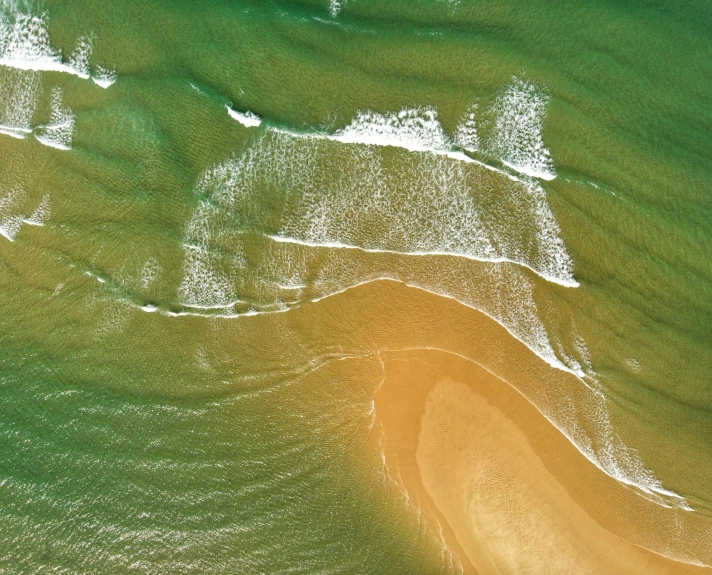 water waves crash on the sand and a green body of water