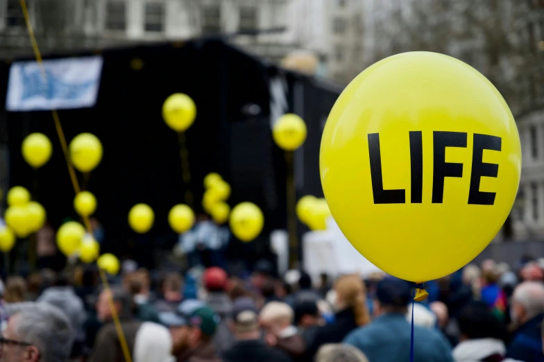 yellow balloons with the words life printed on them are in front of a large crowd