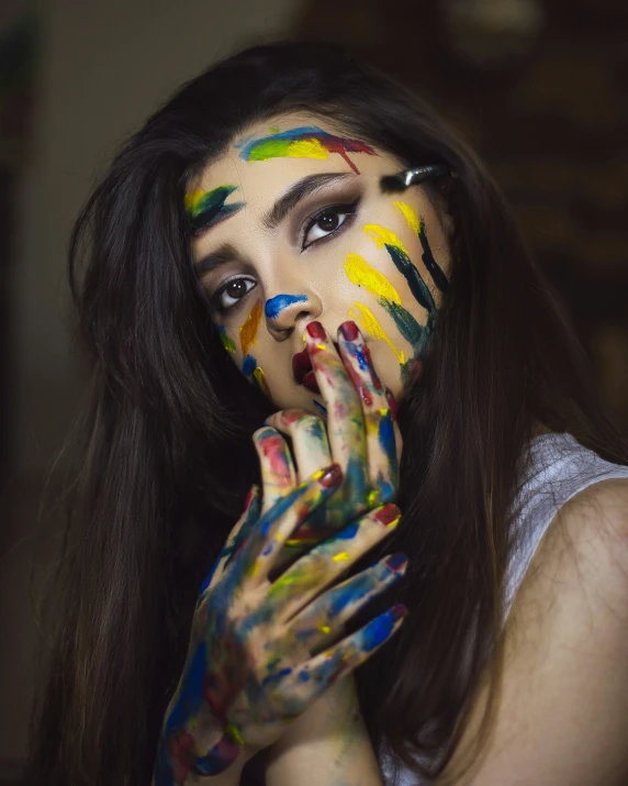 young woman holding her hands to her face with paints all over her face