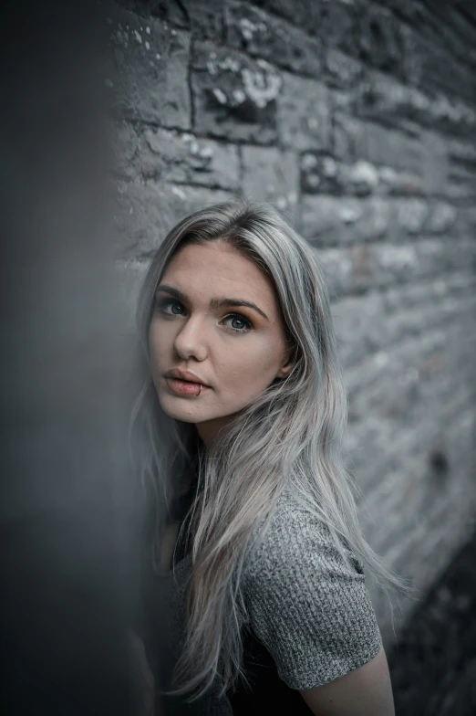 an attractive young woman poses against a brick wall