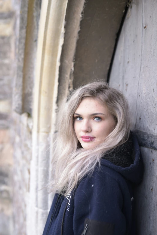 a woman is leaning against a wall and looking into the camera